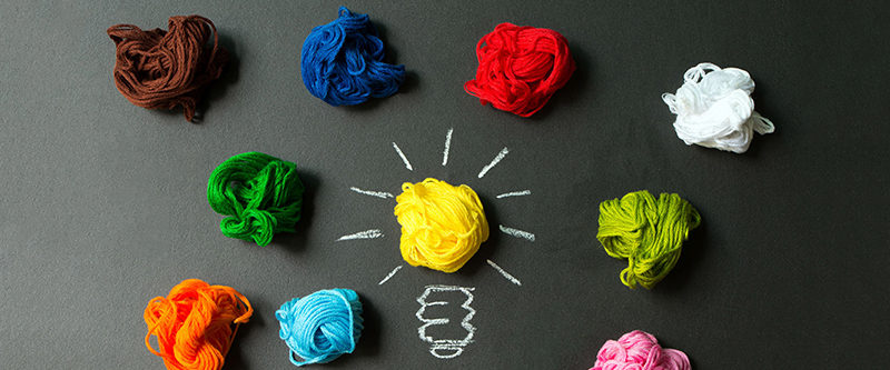 Great idea concept with light bulb among multicolor yarn balls over black background